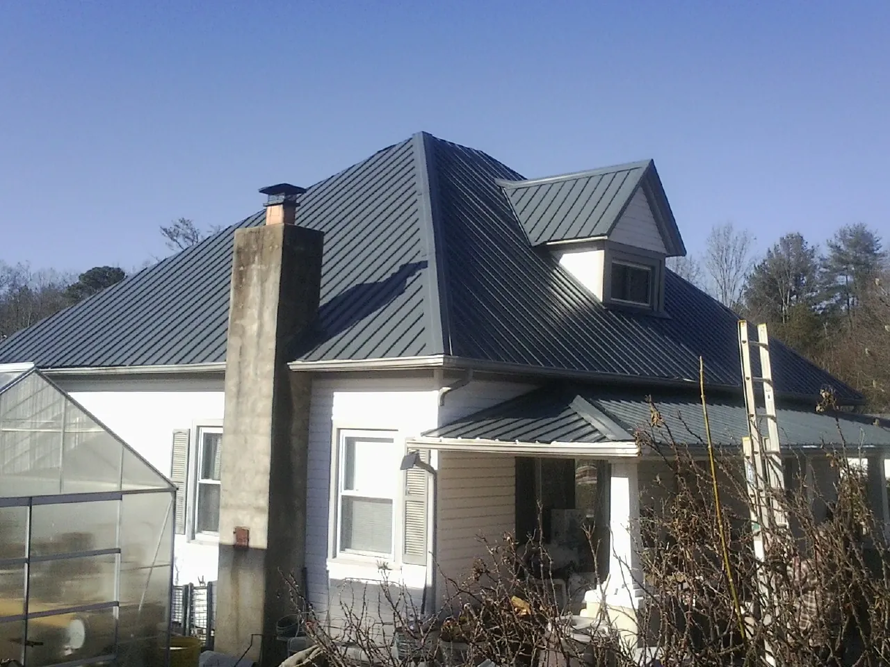 Dark blue standing seam metal roof on a white farmhouse with dormer — Slate & Tile Roof Repair by Roofing Brothers in Belle Rose