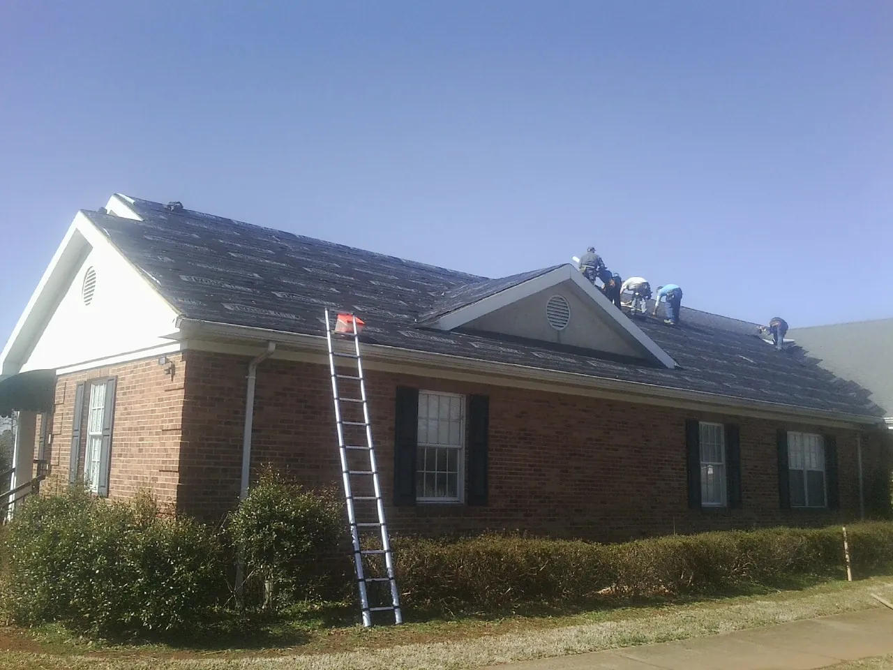 Crew tearing shingles off a brick ranch roof with a ladder set — Metal Roof Repair work by our crew in Belle Rose
