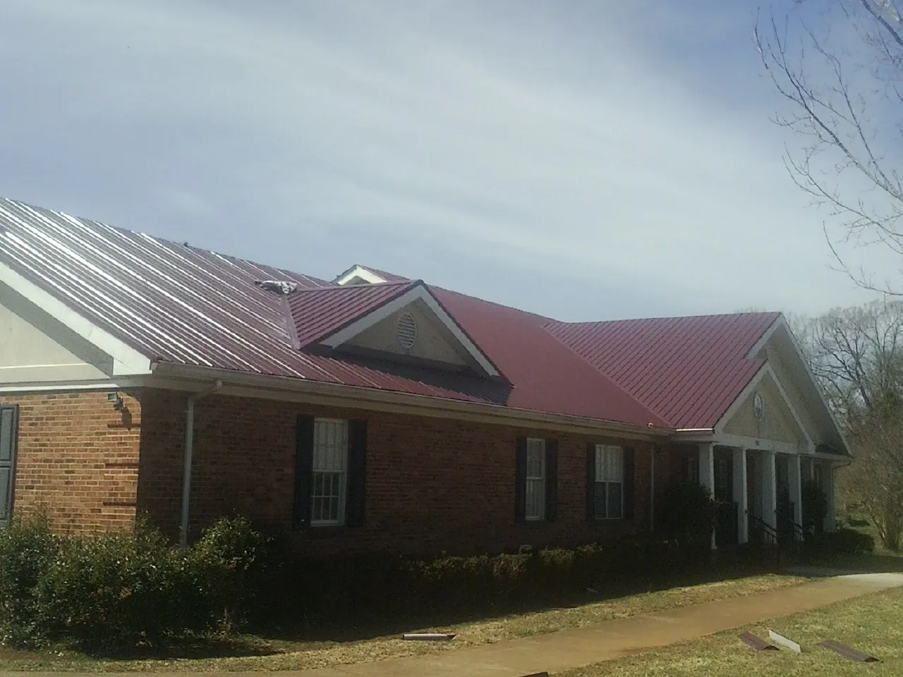 Red metal roof with gabled entries on a long brick building, from a Hail Damage Roof Repair job in Belle Rose