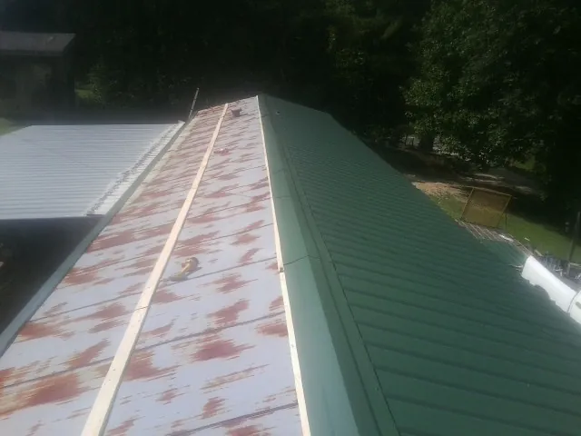 Old rusted panels beside newly installed green metal roofing — Wind Damage Roof Repair by Roofing Brothers in Belle Rose