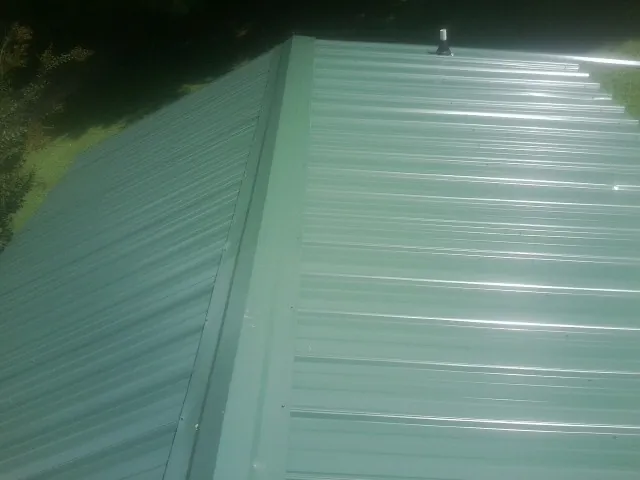 New green metal panels meeting at the ridge of a roof — Flat Roof Repair work by our crew in Belle Rose