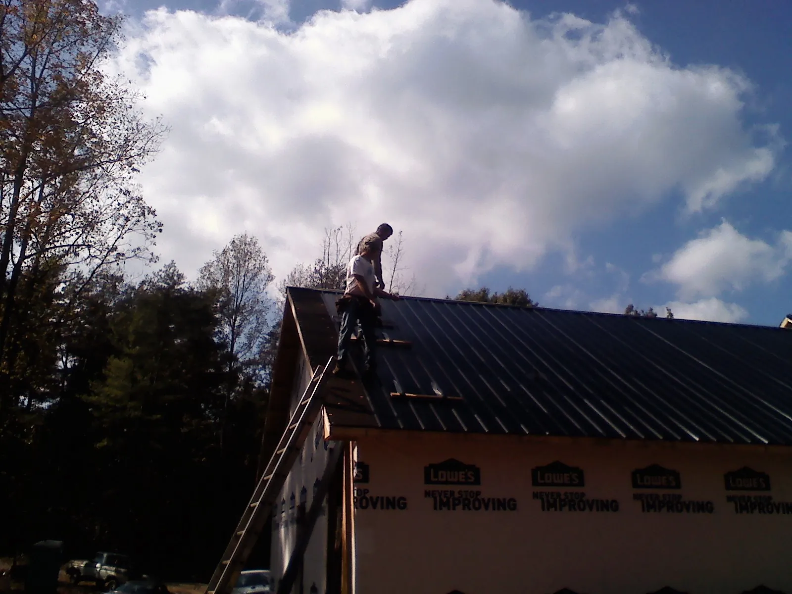 Roofer fastening dark metal panels high against a cloudy sky, from a Roof Inspection job in Belle Rose