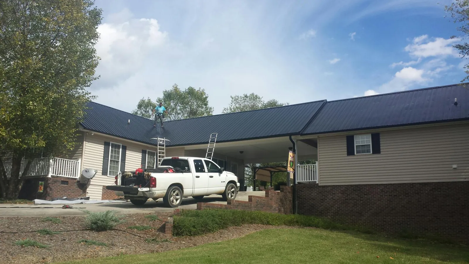 Black metal roof over a home and attached breezeway with ladders set in Belle Rose