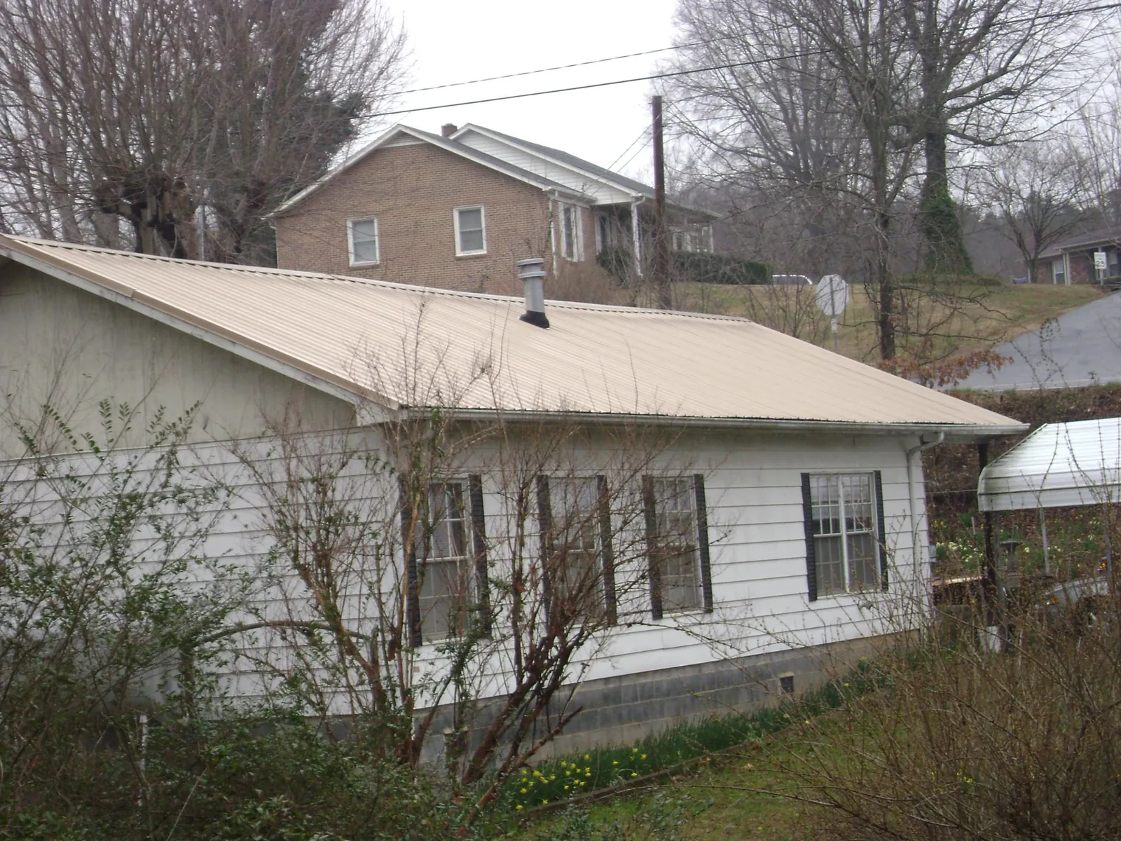 Tan metal roof on a white sided house set into a hillside — Commercial Roofing by Roofing Brothers in Belle Rose
