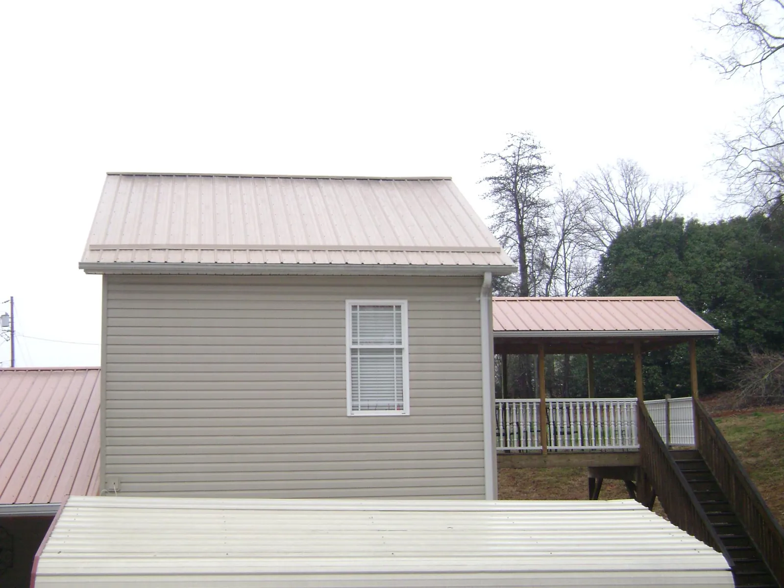 Tan metal roofs on a two story addition and attached porch, from a Roof Replacement job in Belle Rose